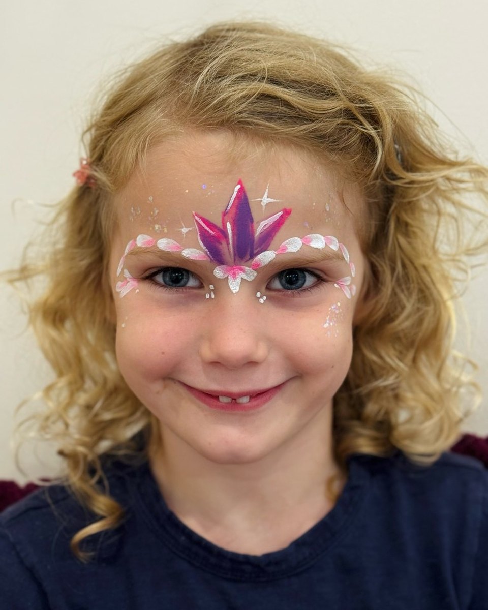 Smiling child with magenta crystal and pink floral crown face painting by Wildflower Face Art