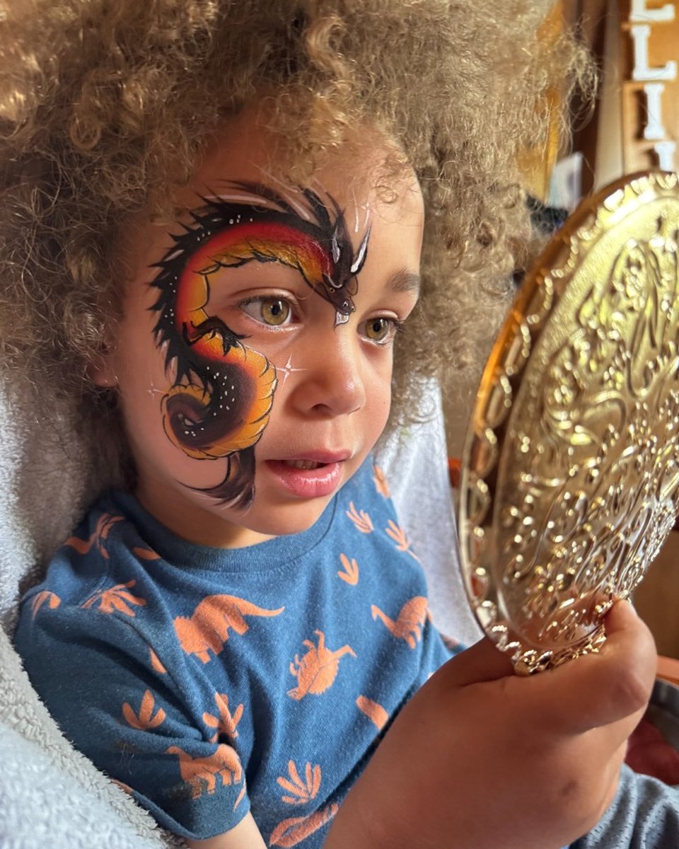 Child with orange and black dragon face painting by Wildflower Face Art